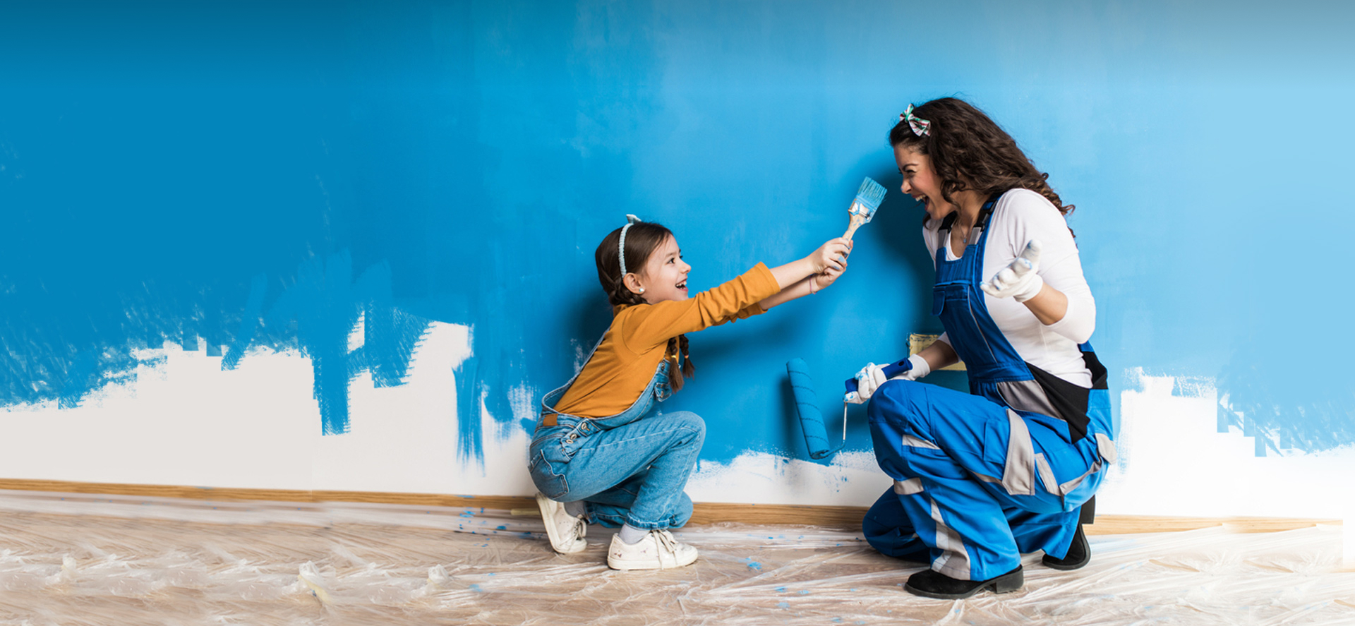 A Little Girl and Her Mother Painting Wall and Smiling at Each Other